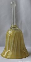 Hand blown glass bell with yellow and white swirled design and clear handle, standing upright on a white backdrop.