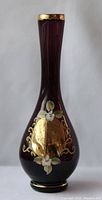 Front view of tall vintage Italian glass vase showing reddish dark color, gold trim, floral and gold shield design.