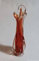 Front view of the tall slender hand blown glass vase displaying fire red and orange swirling colors with a twisted handle and fluted top.