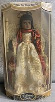 Front view of boxed bisque porcelain doll in cream and gold embroidered gown, red scarf, seated in gold wire chair inside original packaging with 'Collector's Choice' branding.