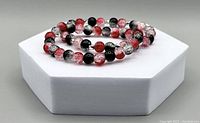 Two crackled glass bead bracelets displayed on a white hexagonal platform showing red, black, and clear beads in a glossy finish.