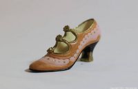 Front and side view of a small vintage handpainted boot heel figurine in pink, gold, peach and black colors.