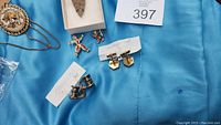 Photo showing the arrowhead pendant in a display box, gold bull oval pendant on chain, two pairs of vintage cufflinks with notes, and two clown pins.