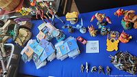 View of the pirate ship Lego set, various character figurines, a small red toy car, stacks of Disney stickers, and colorful collectible figurines placed on a blue surface.