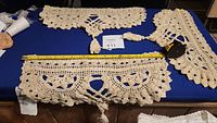 Three cream-colored crocheted doilies with scalloped edges and tassel accents displayed on a dark surface with measuring tape for scale.