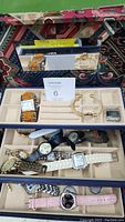 Wide view of the tri-level jewelry box open showing a variety of watches on all levels and a mirror in the lid.