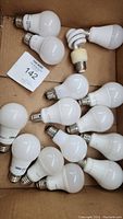 Box containing 15 mixed lightbulbs including round LEDs and a spiral CFL bulb shown in original packaging. Various sizes and wattages visible.