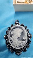 Close-up of dark background cameo pendant with white carved profile of young girl