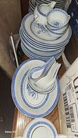 Stack of plates, cups, and soup spoons showing the blue and white rice pattern design, translucent spots visible
