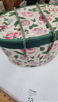 Close-up of floral patterned fabric covered oval sewing box with green cord handles