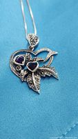 Close-up of the pendant showing two purple heart-shaped amethyst stones set in a sterling silver pendant with marcasite and flowing ribbon design