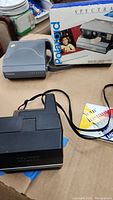 Polaroid Spectra 2 camera shown with its original box and an accessory on a tabletop with some manuals visible