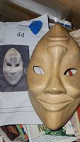 Vintage carved wood drama mask resting on some papers, showing facial details and carved features including painted eye detail