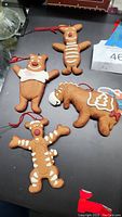Four gingerbread cookie style ornaments on flat surface: Pooh, Piglet, Eeyore, Tigger with red hanging loops