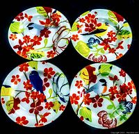 Four glass dinner plates displayed in a 2x2 arrangement, showing colorful bird motifs among floral and leaf designs on a black background.