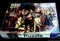 Photo showing the sealed Ravensburger puzzle box front with The Night Watch painting image and branding details visible.
