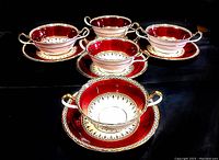 Five Aynsley bouillon cups on matching saucers in a semi-circle on a black background