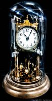 Image of vintage glass dome mantel clock showing brass base, visible clock mechanism inside clear glass dome, white clock face with black numbers.