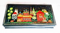 Top view of closed jewelry box showing detailed hand painted village scene in bright colors on black lacquer surface with gold border