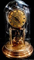 Vintage Kundo mantel clock under glass dome with gold-tone base and decorative clock face and pendulum.