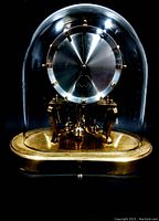 Oblong dome glass mantel clock with brushed silver dial, gold hour markers, and gold-tone base on black background.
