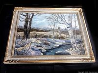 Frontal view of vintage oil painting in ornate golden frame showing winter landscape with creek, trees, and fence.