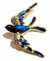 Front side of vintage bird brooch showing detailed blue enamel wings with rhinestones and gold-tone metal.