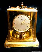 Front and side view of the gold-tone Schatz 1000 day mantel clock with glass sides and pendulum balls.