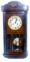 Front view of vintage wooden hand carved wall mount clock showing clock face, wooden frame with carved detail, and pendulum through glass.