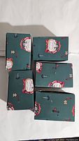 Five boxed Blue Sky Clayworks Christmas ornaments stacked and laid out, green boxes with Santa Claus designs visible.
