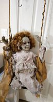 Close-up of the hanging Halloween doll prop seated on the swing, showing the doll's porcelain face, curly brown hair, and vintage dress.