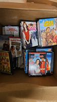 Box of assorted DVDs showing titles Post Grad, Joe Dirt, Great Outdoors, Sydney White, Duplex, and more.