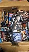 Box filled with over 100 DVDs stacked and loosely packed, showing various black DVD cases with movie artwork.