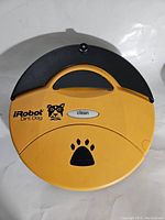 Top view of yellow iRobot Dirt Dog robotic vacuum showing clean button and paw print design