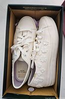 Top view of the white Kate Spade Triple Kick Keds sneaker showing floral applique and lace-up design inside box.