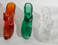 Top view showing color and detailed texture of three glass shoes in amber, green, and clear.