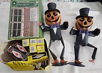 Two pumpkin-headed figurines in tuxedos and top hats, box of Sato black flame flicker candles, and Holiday Time 8-foot Ribbon Light Set.