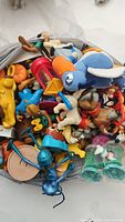 Pile of assorted Disney toys showing various characters including Donald Duck, Blue Fairy, and other plush and plastic figurines.