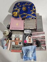 Overview of all products showing a blue pouch with gold chain designs, boxed skincare masks, dark circle under eye gels, Biore pore strips, makeup sponge items, and various small bottles and makeup items.