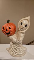 Side view of vintage ceramic ghost holding pumpkin, showing draped cloak and pumpkin detail