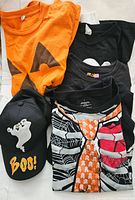Lot contents showing five Halloween-themed T-shirts and one black cap with Halloween motifs.