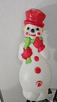 Full view of vintage snowman blow mold showing red hat, green scarf, red gloves, and smiling face