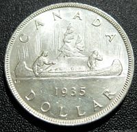 Close-up of the reverse side of the 1935 Canada silver dollar coin showing two men paddling a canoe with trees in the background, date 1935, and inscriptions CANADA DOLLAR.