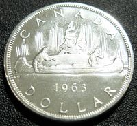 Obverse side of the 1963 Canadian silver dollar coin showing the canoe with two figures, the year, and country name.