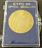 Closed view of the Expo 86 medallion housed in its clear plastic case with blue felt backing and gold lettering.