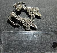 Close-up of Sherman earrings with clip-on backs and decorative stones, next to ruler showing size approximately 1.5 inches long.