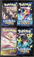 Front view of four Pokémon trading card booster packs in sealed packaging, three labeled Shining Fates and one Champion's Path.
