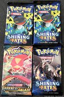 Front view of four Pokémon trading card booster packs including three Shining Fates and one Darkness Ablaze.