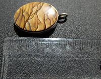 Top view of the pendant next to a ruler to show size, approximately 1.5 inches tall including loop, gemstone is about 1.25 inch oval.