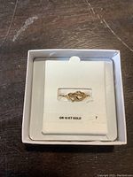 Photo showing the 10 KT gold double heart ring placed on a white display card inside a small white box. The ring features two intertwined open hearts.